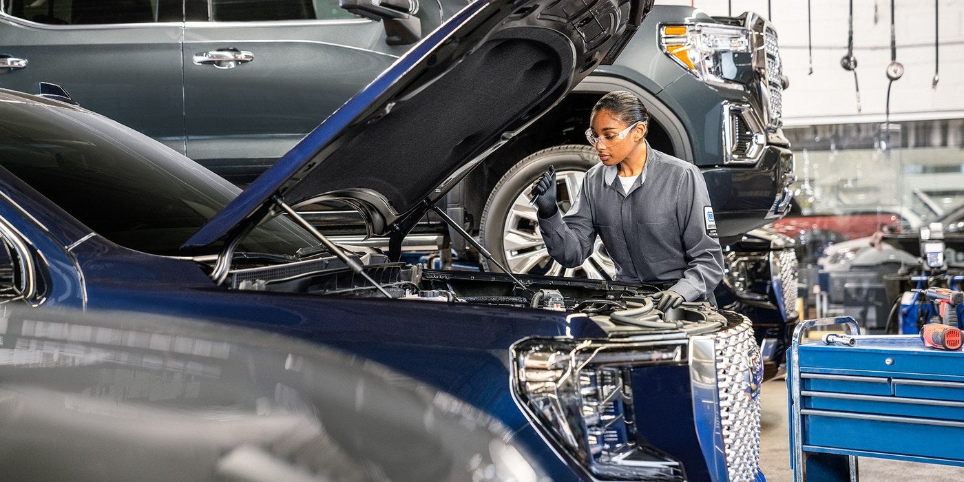 GMC Certified Service technician checking the engine of a blue GMC truck for an oil change in Graham, TX