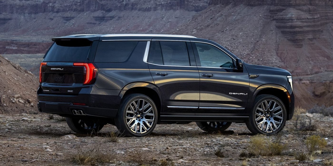 Dark GMC Yukon SUV parked on rocky ground with mountains behind it
