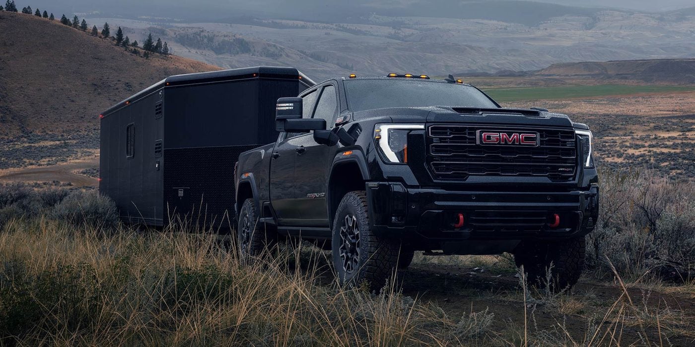 Black GMC Sierra HD pickup towing a camper trailer across open country