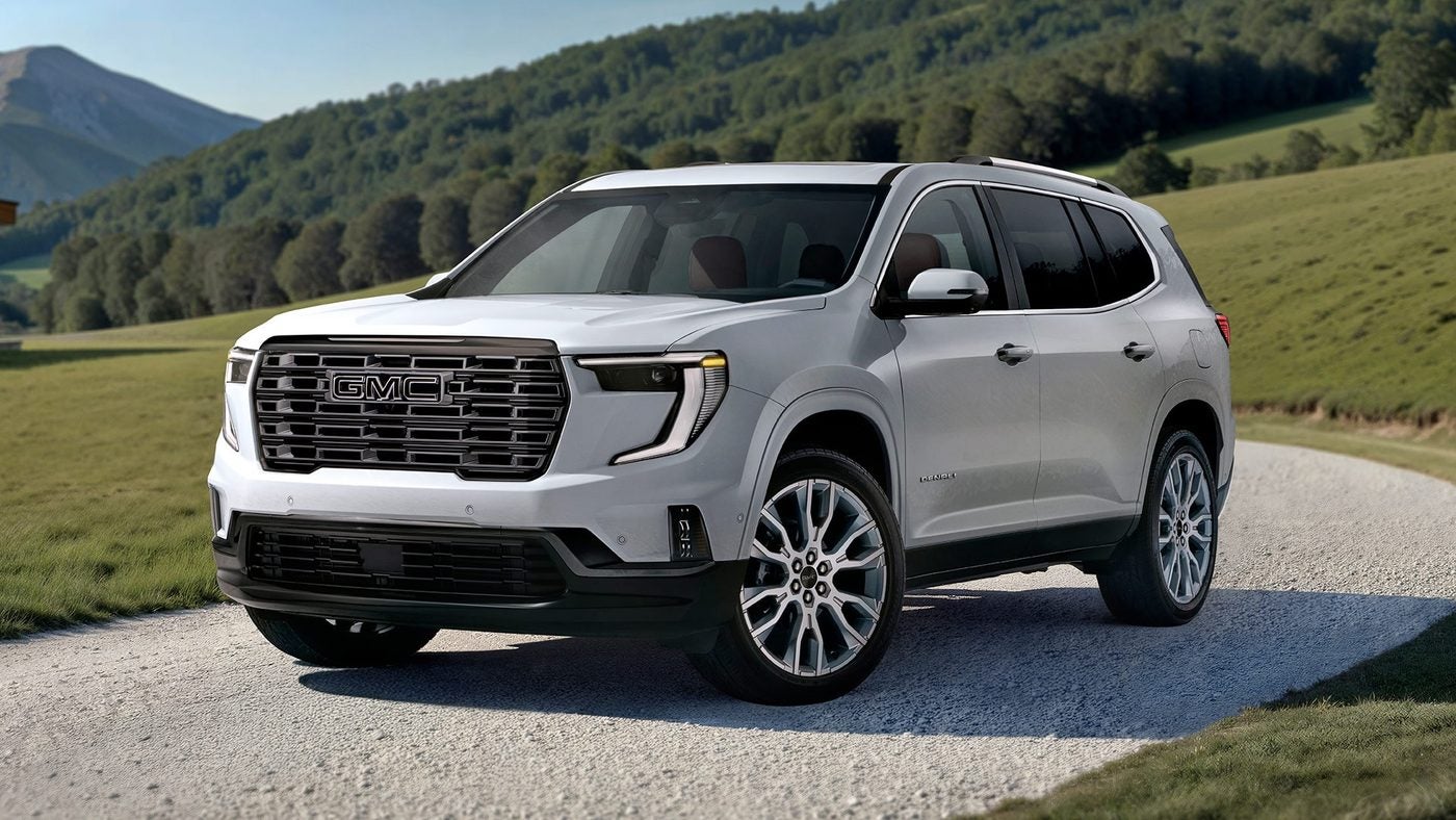 White GMC Acadia SUV on a gravel road with green hills in the background