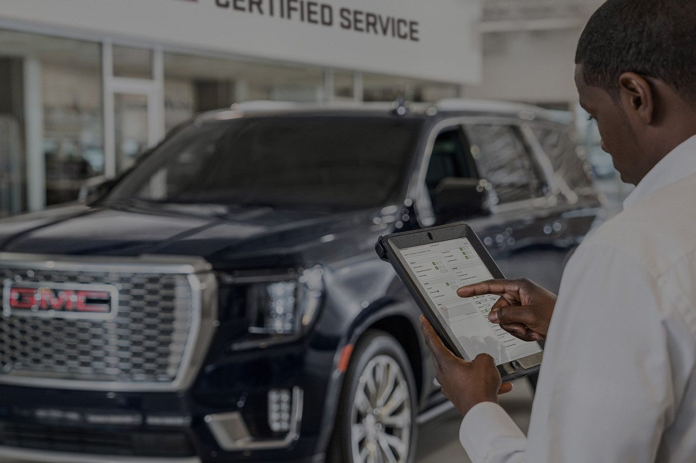 Service advisor using a tablet beside a GMC Yukon at the Certified Service area of a GMC dealership