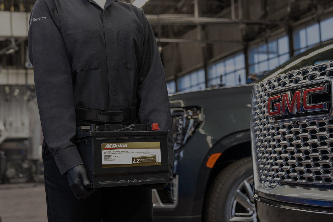 Technician holding an ACDelco battery beside the Denali grille of a GMC at Holiday GMC in Graham, TX