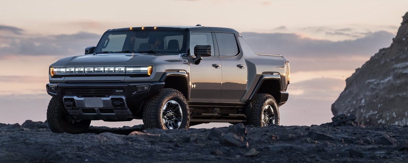 GMC HUMMER EV pickup parked on dark volcanic rock at sunset